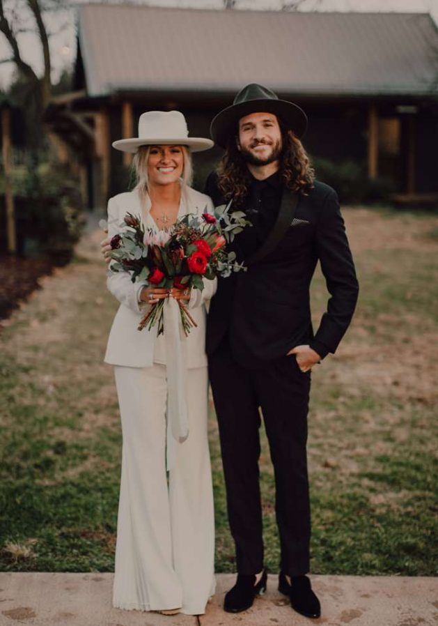 a modern boho bride wearing a white pansuit with a white shirt, a white hat and platform heels