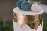 57 a white wedding cake with gold leaf, blue and white macarons and eucalyptus looks very edgy
