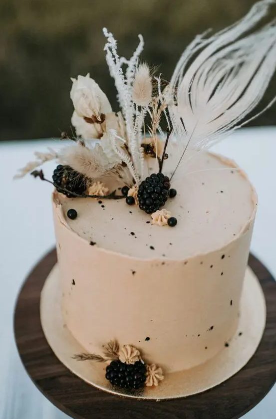 a neutral buttercream wedding cake with speckles, blackberries and dried blooms and grasses