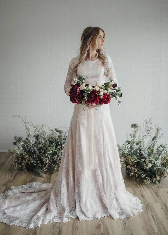 a blush wedding dress with white lace appliques, a train and long sleeves looks feminine