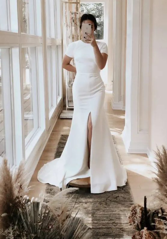 an ultra-modern plain fitting wedding dress with a high neckline, short sleeves, a front slit and a train for a minimalist bride