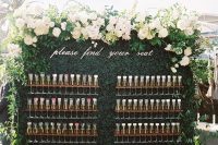 a alrge boxwood champagne wall with wooden holders, greenery and lush white blooms on top plus calligraphy is cool