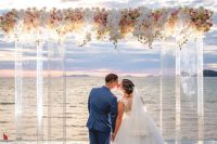a beautiful wedding ceremony space with a sea view, a lucite wedding arch covered with white and pink blooms and with lights
