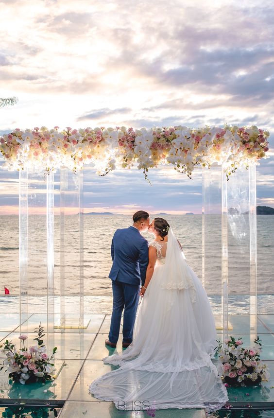 a beautiful wedding ceremony space with a sea view, a lucite wedding arch covered with white and pink blooms and with lights