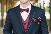 a black tuxedo with silk rim lapels and a bold floral pocket square with red blooms, berries and greenery that matches the waistcoat and the bow tie