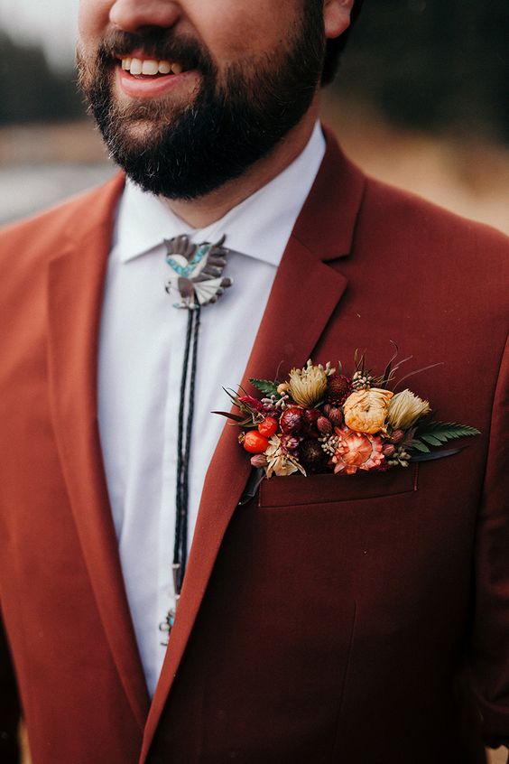 a bold rust blazer and a pocket square with burgundy, yellow and rust blooms, berries and leaves for a fall boho wedding