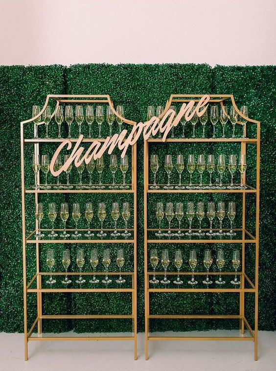 a champagne wall organized of two brass shelving units with glass shelves, a gold calligraphy topper