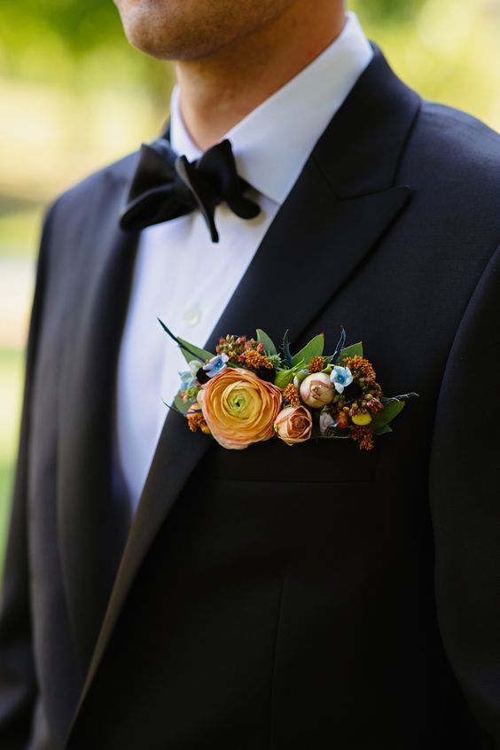 a classic black tux and a bold pocket square styled with peachy, rust and blue flowers, greenery and thistles is wow