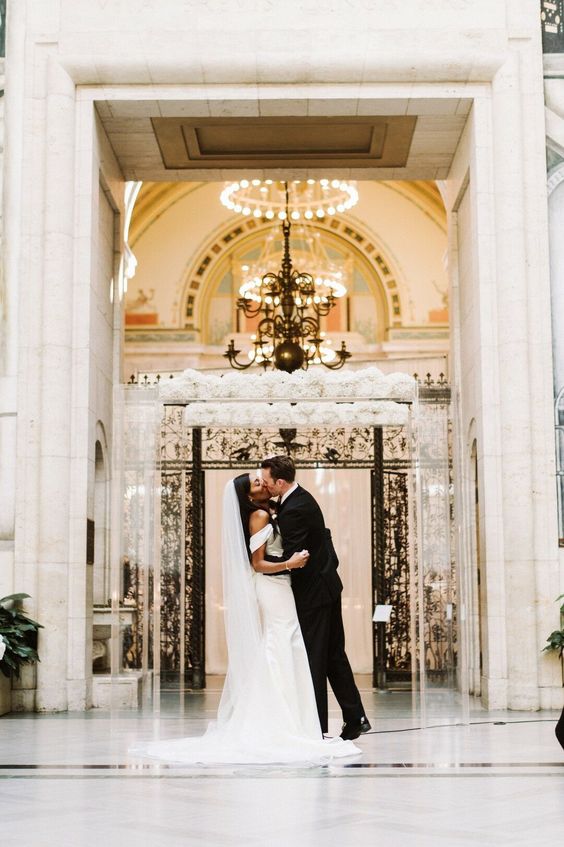 a clear acrylic wedding arch topped with two rows of lush white blooms is a gorgeous idea for a modern luxurious wedding
