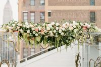 a clear acrylic wedding arch with branches inside it and lush greenery and florals on top the arch plus pillar candles around it