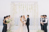 a clear lucite wedding arch with white blooms hanging down from it that seem floating in the mid-air plus a sea view