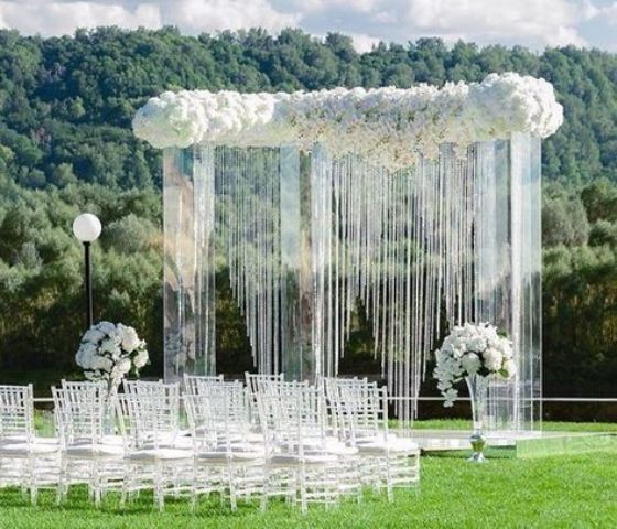 a fabulous acrylic wedding arch with lush white florals on top and some shiny crystals hanging down for a glam wedding