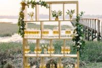 a gilded frame decorated with greenery and white blooms as a champagne wall for a modern glam wedding