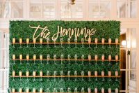 a greenery champagne wall with stained holders, gold calligraphy and a chic gold cart with decor next to it