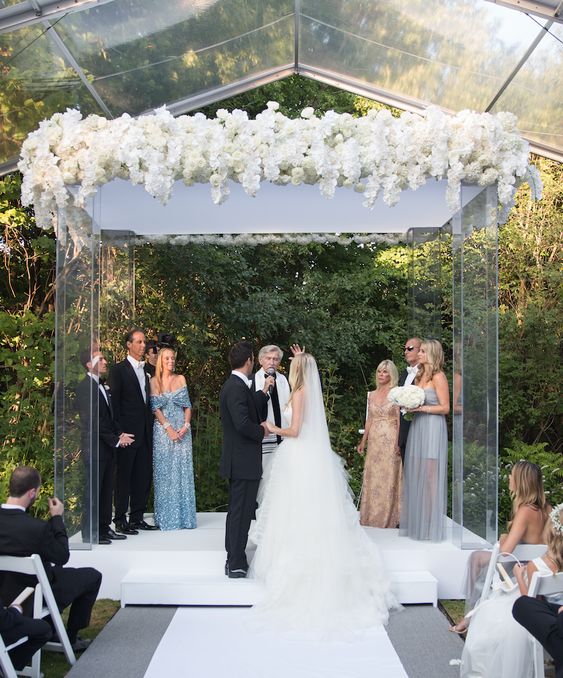 a large lucite wedding arbor topped with very lush white blooms is a beautiful idea for a modern edgy wedding with a lux feel