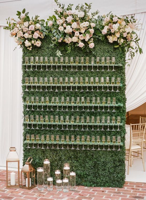 a lovely boxwood wall with pastel floral arrangements on top and green flute holders, floating candles and candle lanterns