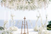 a luxurious wedding ceremony space with a sea view, an acrylic arbor with white blooms covering its top and the pillars, pillar candles