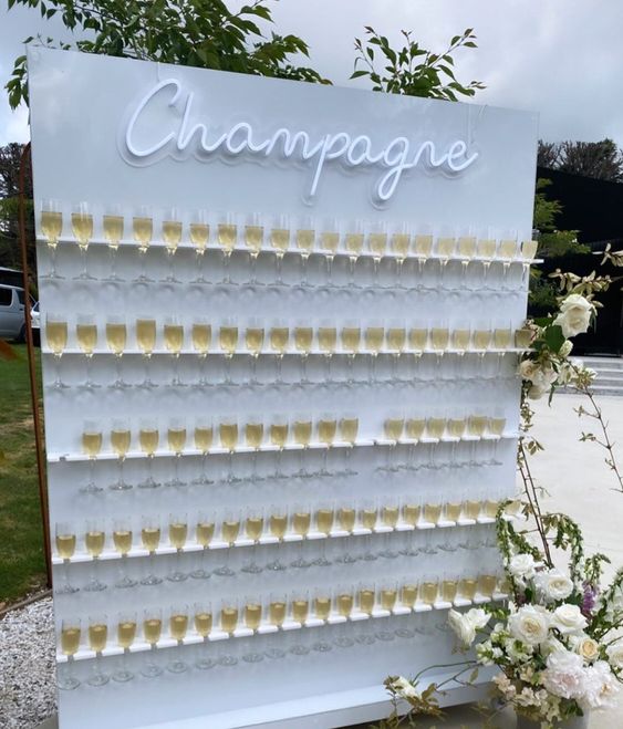 a modern glam champagne wall in white, with matching holders and a neon sign is a pretty idea for a modern wedding