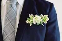 a navy blazer, a grye and navy plaid tie, a fresh pocket square with white and green blooms and succulents for a bolder look
