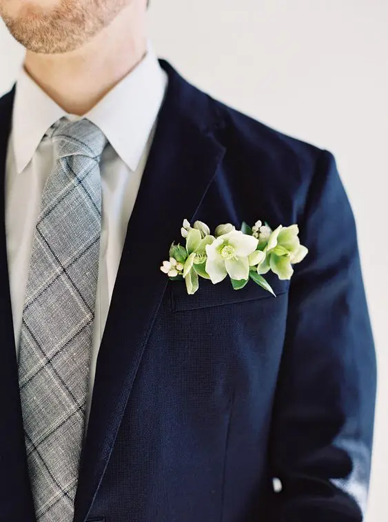 a navy blazer, a grye and navy plaid tie, a fresh pocket square with white and green blooms and succulents for a bolder look