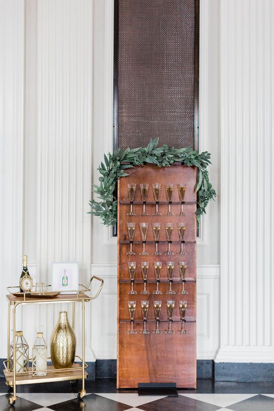 a small and chic wedding champagne copper wall with metal holders and a greenery garland on top is a bold solution
