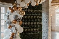 a small boxwood wedding champagne wall with dark-stained holders, a white, silver and gold balloon garland covering it