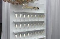 a super glam champagne wall of white plywood, with shelves, an acrylic calligraphy sign, a pastel floral arrangement with pampas gras