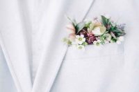 a white tux with a pocket square done with hellebores, wax flower and tight red buds plus greenery for a slight pastel touch