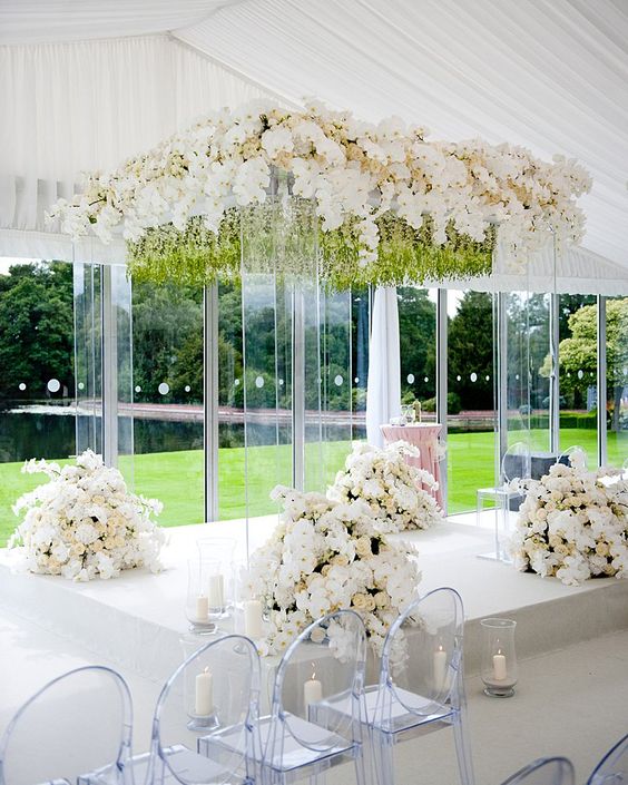 an acrylic wedding arch done with greenery and neutral blooms, with white floral arrangements at the base of the arch
