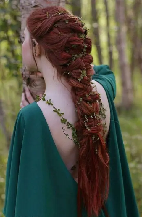 an elvish bridal look with a green dress with a deep cut back, with a large twisted braid and greenery touches