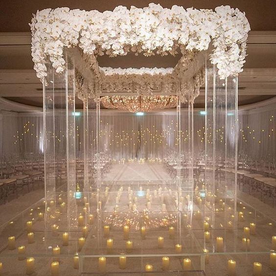 an outstanding lucite wedding arbor topped with lush white orchids and with a clear floor with candles right under the arbor
