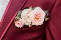 an oxblood blazer with catchy lapels and a pocket square styled with blush and neutral blooms, leaves and some mauve touches