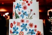 05 a white buttercream wedding cake with uneven edges and red and blue pressed flowers and leaves to form a pattern and a color scheme