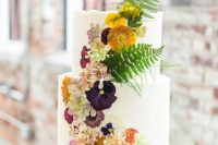 06 a white buttercream wedding cake with uneven edges and bold mustard, pink and deep purple blooms pressed and some leaves standing out for a fall wedding