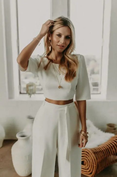 a modern bridal look with a plain crop top with short sleeves and high waisted pants with a sash, statement earrings and some more jewelry