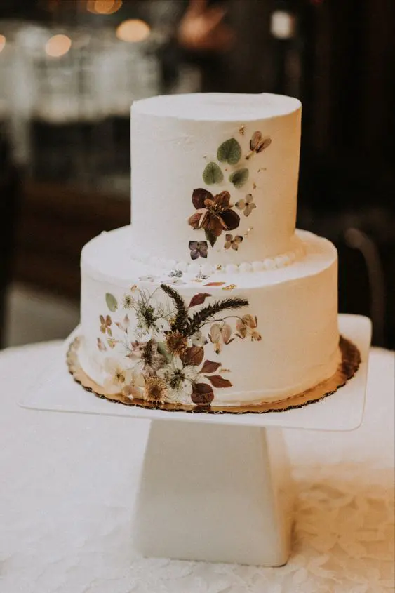 a stylish and trendy white buttercream wedding cake with pressed dried flowers and leaves composes two trends in one