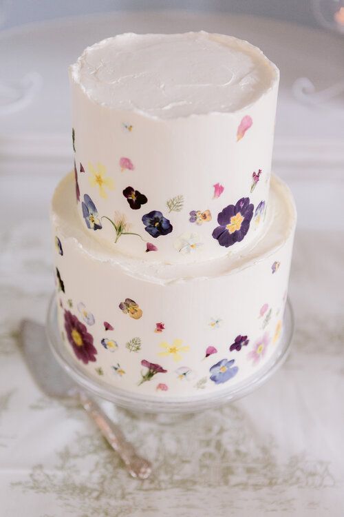 a delicate white buttercream wedding cake with a rough edge and a bit of mauve, purple and blue and yellow blooms pressed to form a pattern