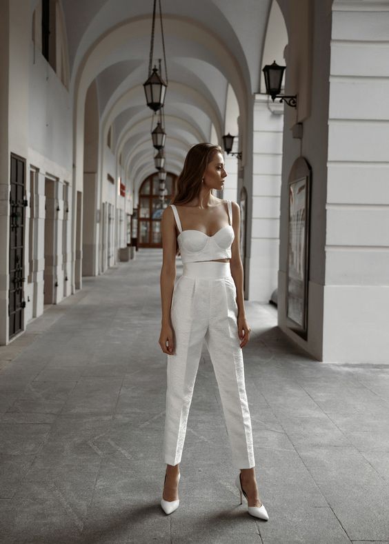 a sexy bridal look with a croset like crop top and high waisted cropped trousers, white heels and pearl earrings