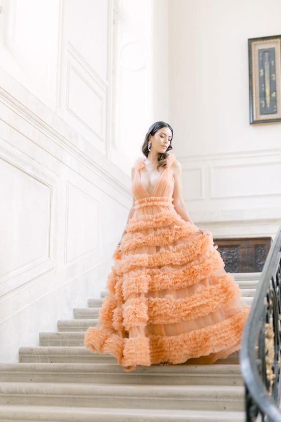 a bold orange A-line wedding dress with a tulle bodice, a plunging neckline, a ruffle tier skirt and statement earrings