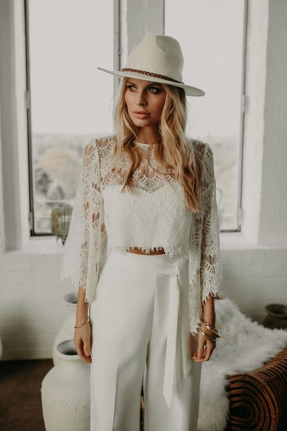 a beautiful boho bridal look with a plain crop top and a lace long sleeve one over it, plain high waisted pants, a white hat