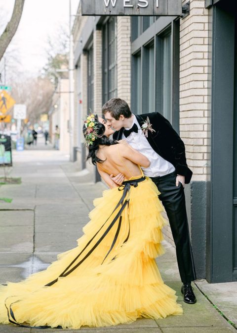 a bold sunny yellow A-line wedding dress with spaghetti straps, an open back and a tiered ruffle skirt with a train plus a black ribbon belt