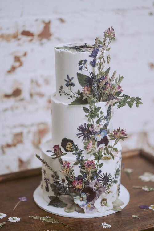 a white buttercream wedding cake with an uneven edge and pressed dried and fresh blooms plus flowers attached to the cake for a 3D effect