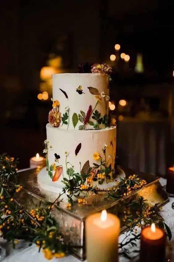 a white buttercream wedding cake with bold blooms and greenery pressed to the cake is a decadent and refined idea for a fall wedding
