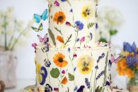 27 a fantastic white buttercream wedding cake with uneven edges, colorful pressed flowers and leaves and colorful butterflies as cake toppers