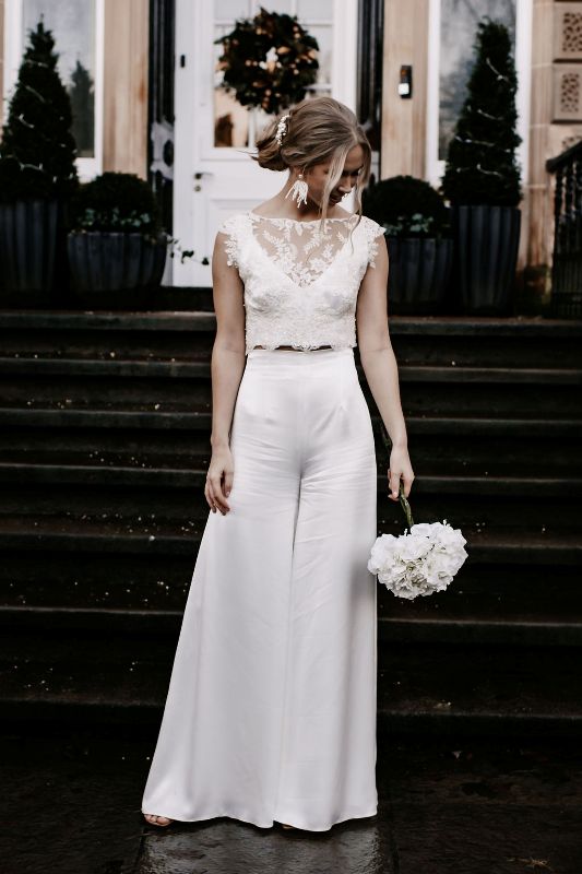 a refined modern bridal outfit with a plain crop top, high waisted wideleg and flare pants, statement earrings and a pearl headpiece