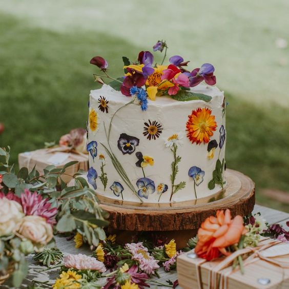 a one-tier buttercream wedding cake with bright pressed blooms and leaves and more bright flowers on top