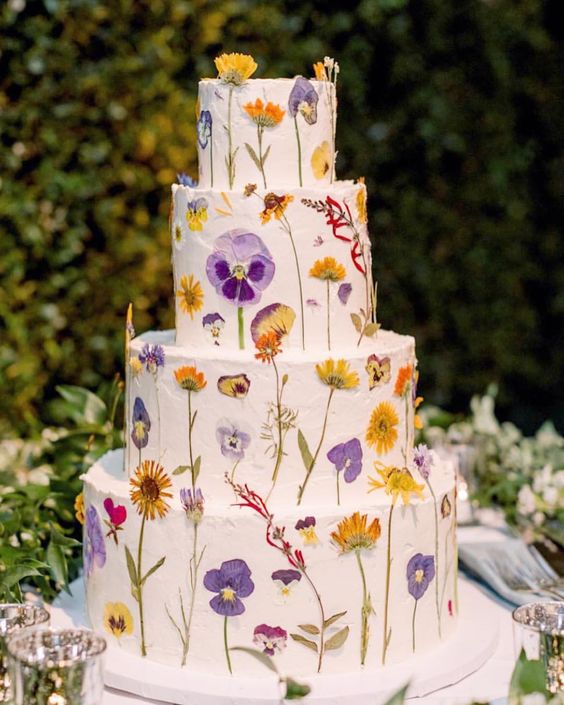 a pretty multi tier white buttercream wedding cake with bright pressed flowers and leaves is a fun and cool idea for spring and summer weddings
