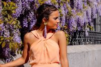 33 a soft orange jumpsuit with a catchy neckline, lilac tassel earrings and a lilac clutch with a tassel for a spring or summer garden wedding
