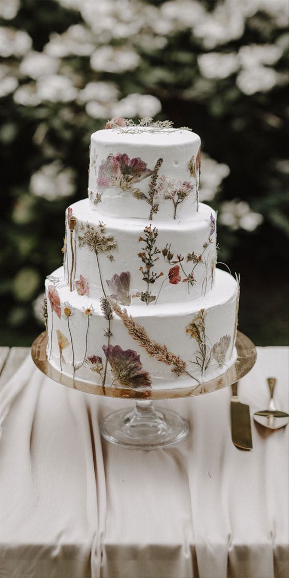 a subtle white buttercream wedding cake with pressed dried flowers and herbs is a lovely idea for a boho wedding