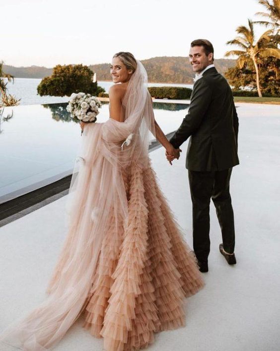 a jaw dropping peachy pink A line wedding dress with a ruffle skirt and a neutral veil for a statement bridal look